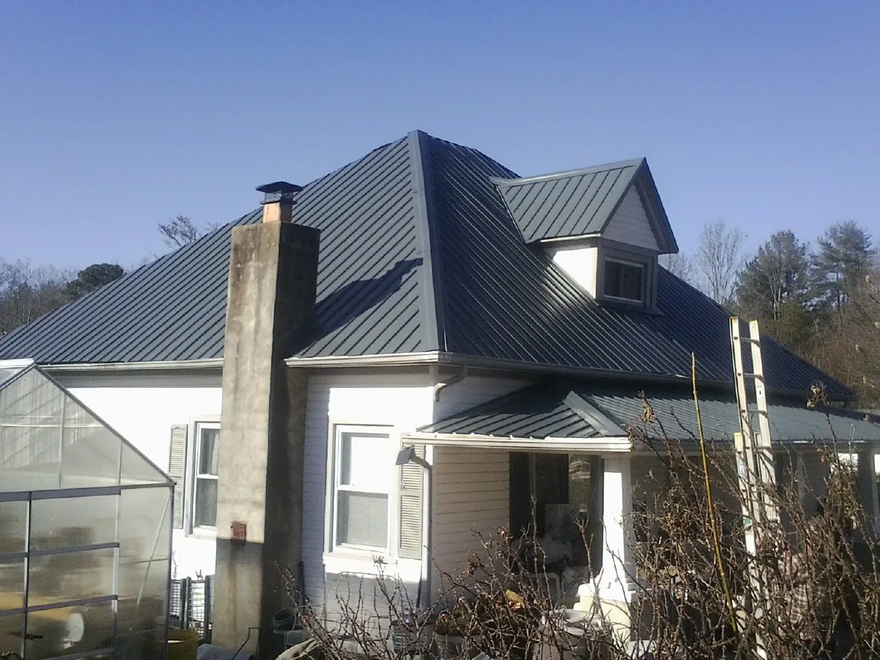 Dark blue standing seam metal roof on a white farmhouse with dormer — Slate & Tile Roof Repair by Roofing Brothers in Brothers