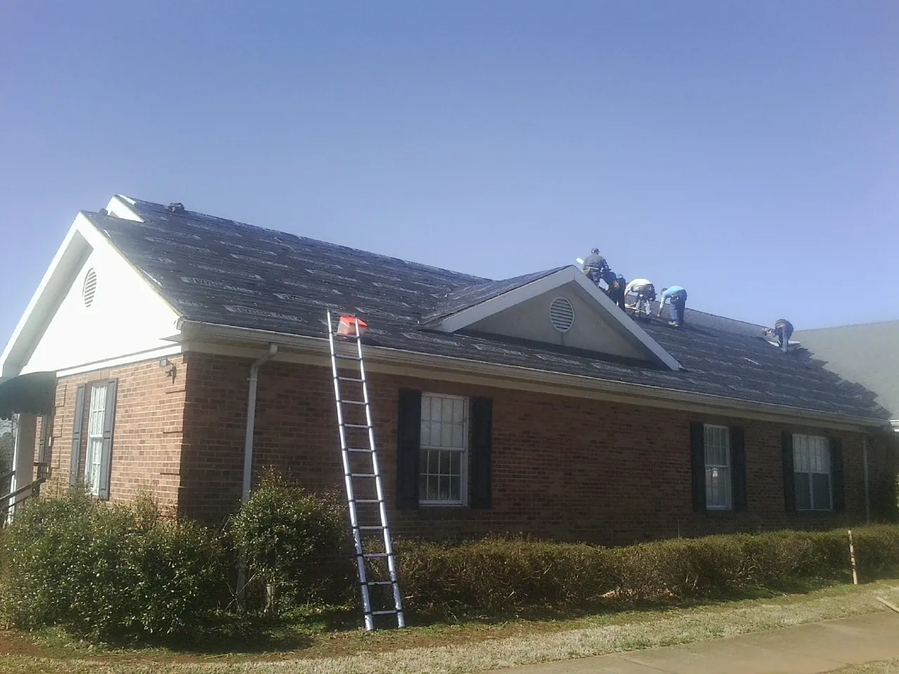 Crew tearing shingles off a brick ranch roof with a ladder set — Emergency Roof Repair work by our crew in Brothers