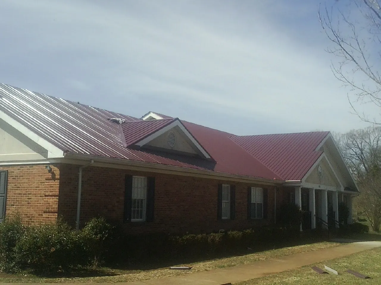 Red metal roof with gabled entries on a long brick building, from a Hail Damage Roof Repair job in Brothers