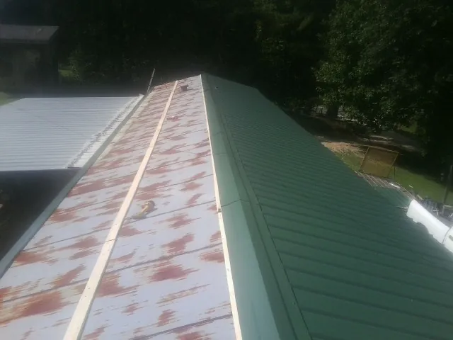 Old rusted panels beside newly installed green metal roofing — Wind Damage Roof Repair by Roofing Brothers in Brothers