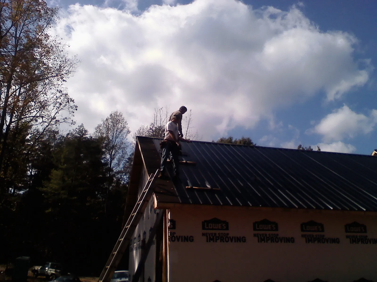 Roofer fastening dark metal panels high against a cloudy sky, from a Roof Inspection job in Brothers