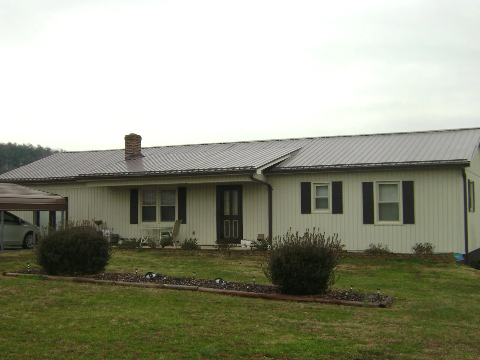 Brown metal roof on a cream sided ranch home with a brick chimney in Brothers