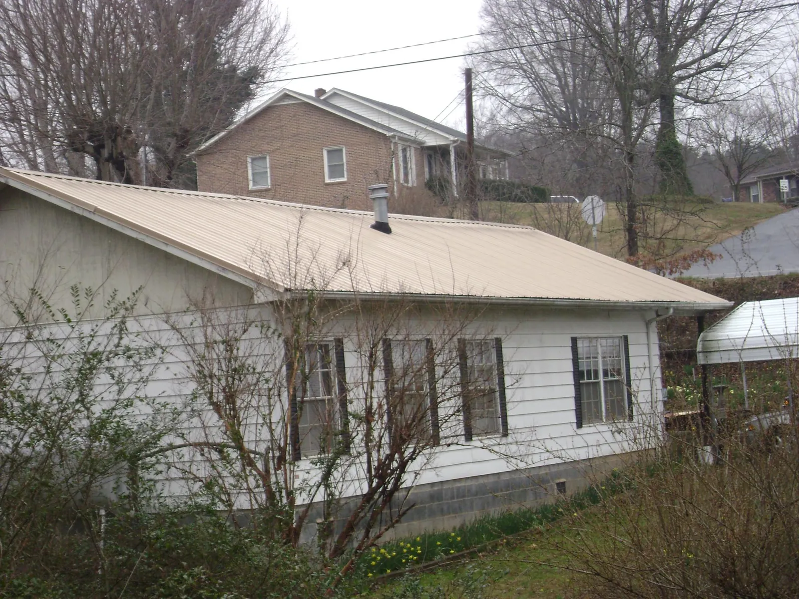 Tan metal roof on a white sided house set into a hillside — Commercial Roofing by Roofing Brothers in Brothers