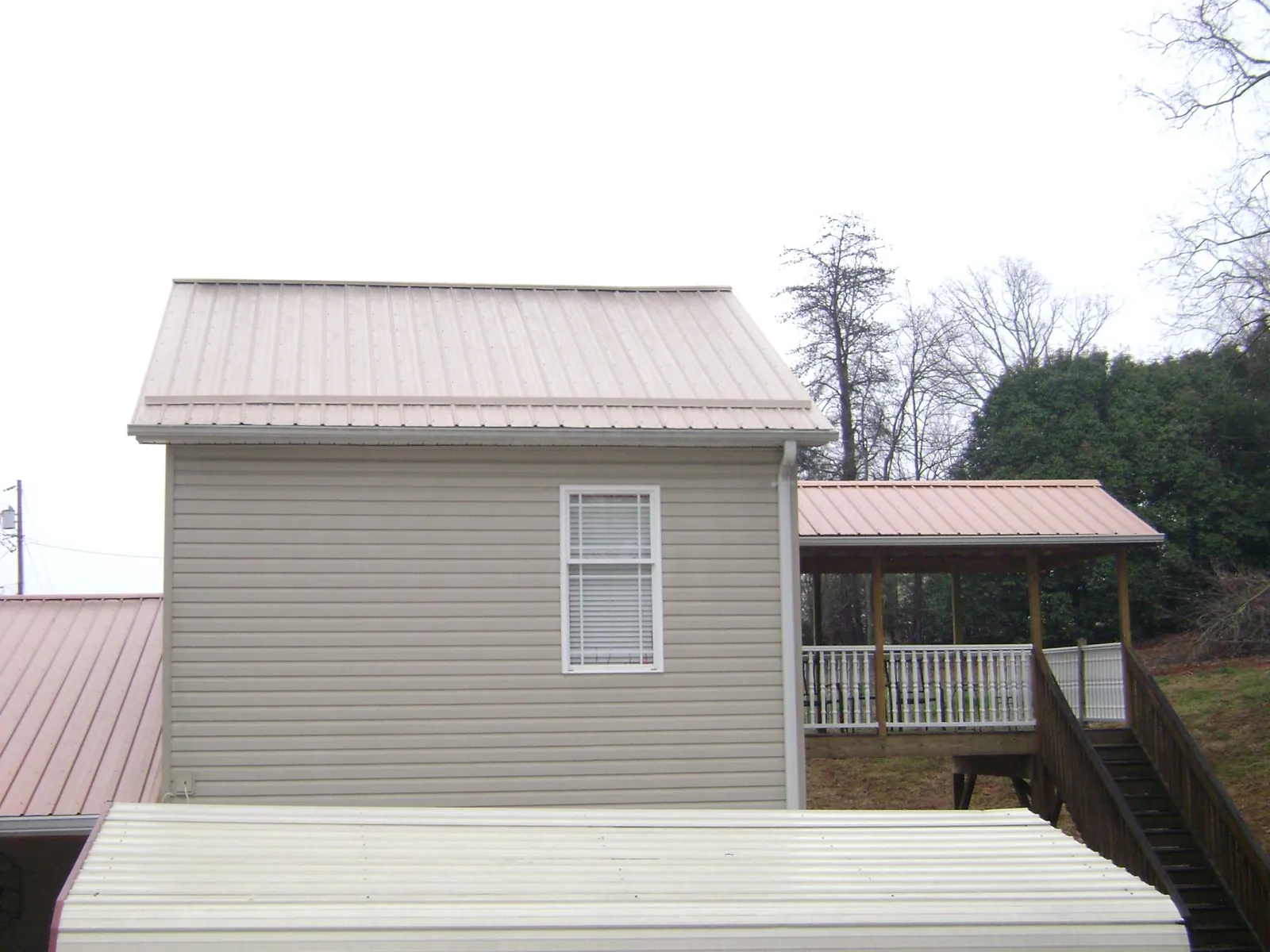 Tan metal roofs on a two story addition and attached porch, from a Roof Replacement job in Brothers